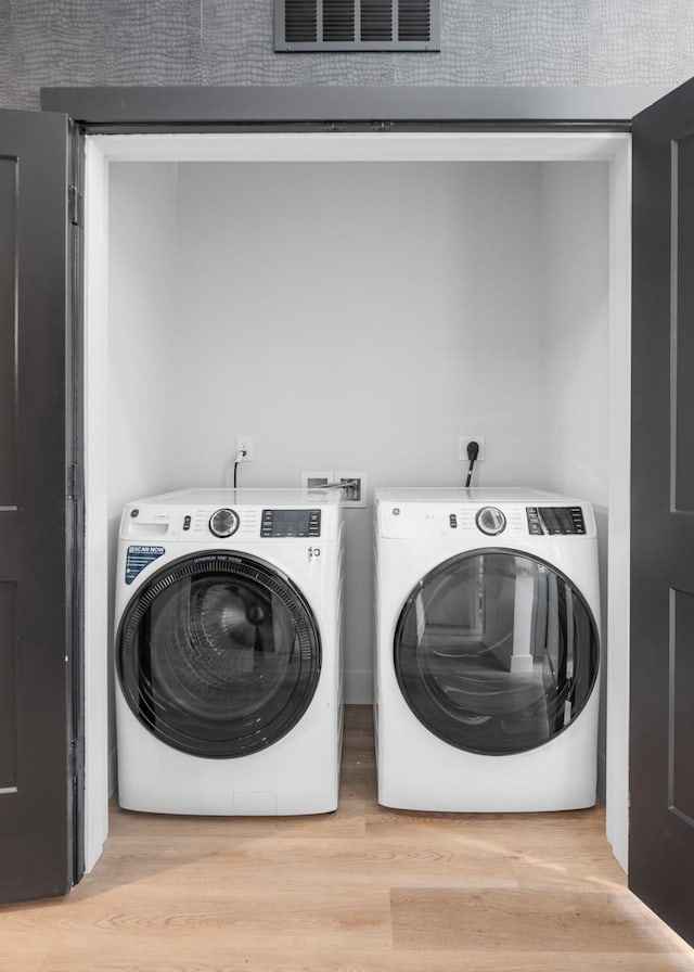 clothes washing area featuring laundry area, visible vents, washer and clothes dryer, and light wood-style floors