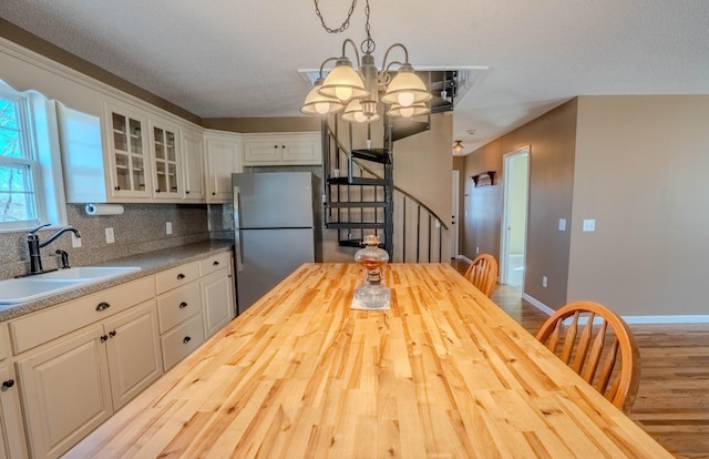 kitchen with butcher block countertops, a sink, backsplash, freestanding refrigerator, and glass insert cabinets