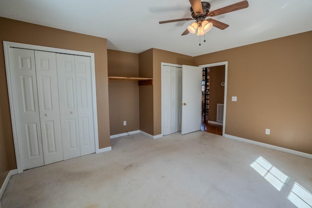 unfurnished bedroom featuring carpet floors, multiple closets, visible vents, a ceiling fan, and baseboards