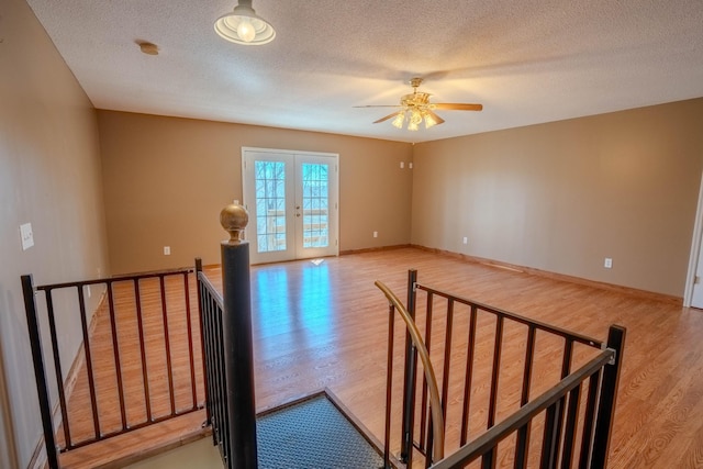 spare room featuring light wood finished floors, baseboards, a textured ceiling, and french doors