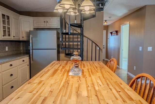 kitchen featuring wood finished floors, wood counters, baseboards, freestanding refrigerator, and glass insert cabinets