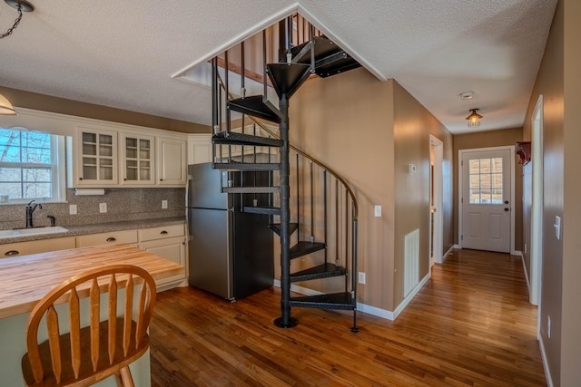 kitchen with butcher block countertops, a sink, freestanding refrigerator, plenty of natural light, and glass insert cabinets