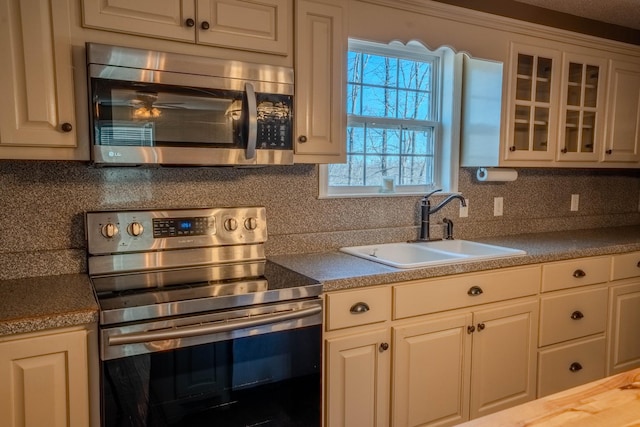 kitchen with tasteful backsplash, white cabinets, glass insert cabinets, appliances with stainless steel finishes, and a sink