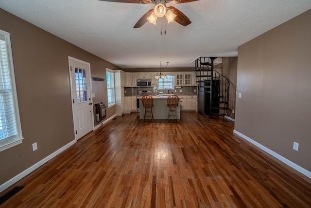 unfurnished living room featuring ceiling fan with notable chandelier, dark wood-style flooring, visible vents, stairway, and heating unit