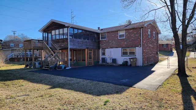 rear view of house featuring cooling unit, brick siding, a sunroom, stairs, and a yard