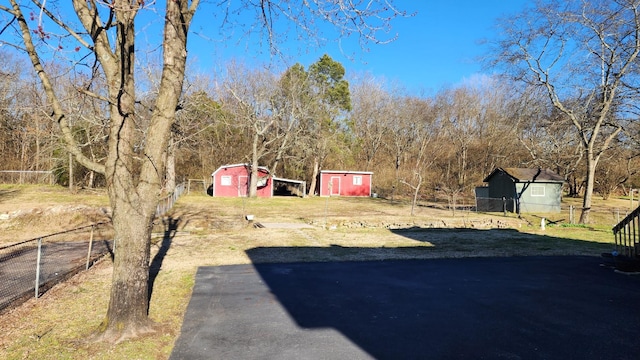 view of yard featuring a detached garage, fence, a shed, an outdoor structure, and driveway