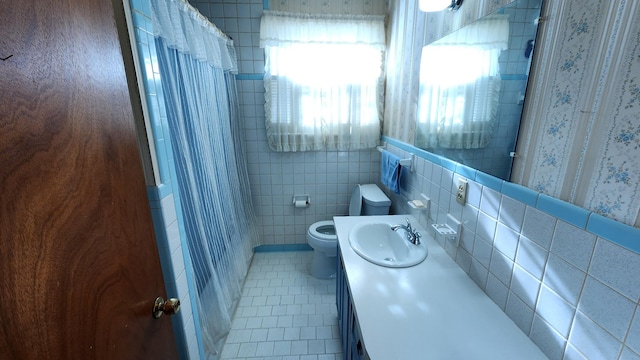 bathroom with toilet, curtained shower, tile patterned flooring, vanity, and tile walls