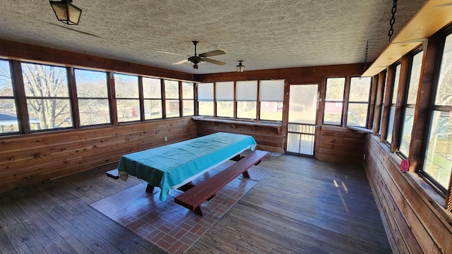 recreation room with a textured ceiling, wood-type flooring, a ceiling fan, and wooden walls