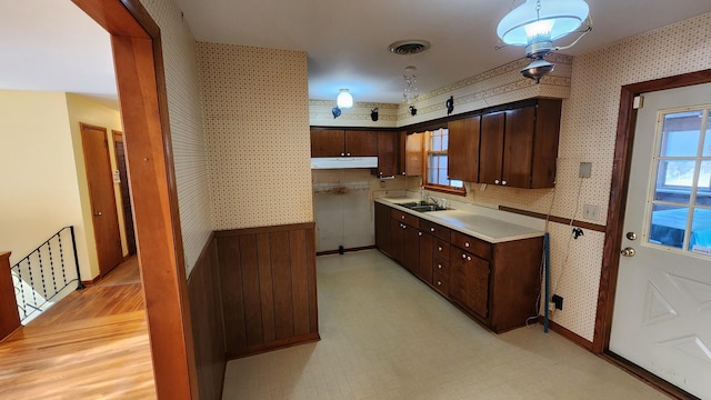 kitchen featuring light floors, visible vents, a sink, under cabinet range hood, and wallpapered walls