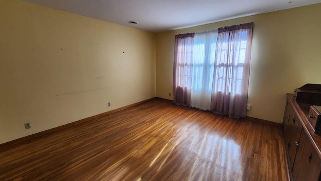 empty room with baseboards, visible vents, and wood finished floors