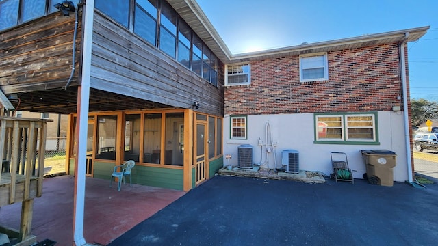 rear view of house featuring a sunroom, brick siding, a patio, and central AC