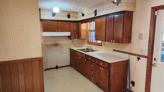 kitchen with wallpapered walls, under cabinet range hood, light countertops, and a sink