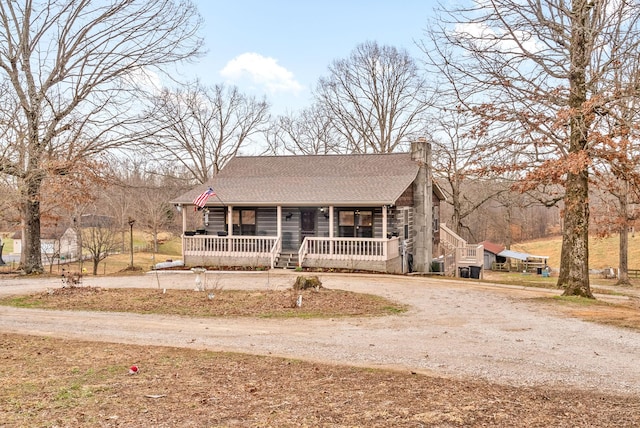 log-style house featuring roof with shingles, a chimney, covered porch, log siding, and driveway