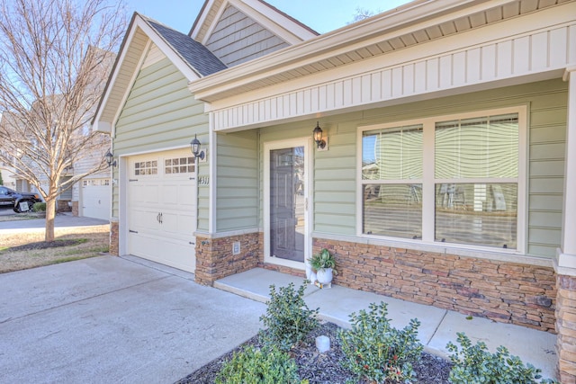 entrance to property with a shingled roof, stone siding, an attached garage, and concrete driveway