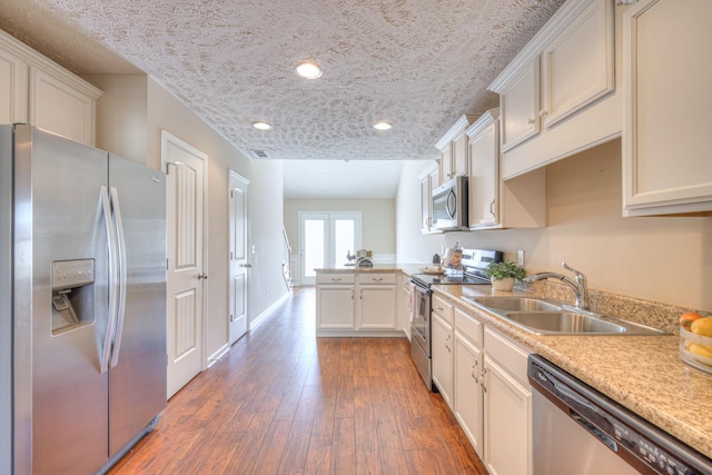 kitchen featuring dark wood-type flooring, a peninsula, stainless steel appliances, light countertops, and a sink