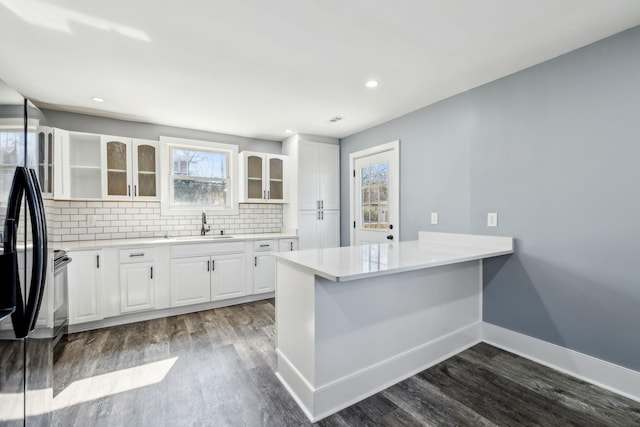 kitchen with dark wood-style flooring, tasteful backsplash, glass insert cabinets, white cabinetry, and baseboards