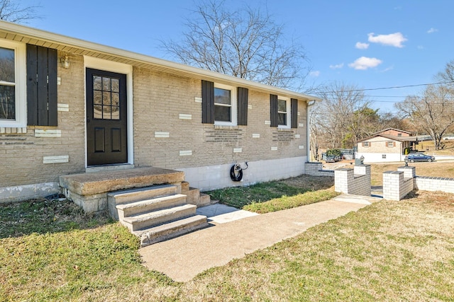 entrance to property with a yard, brick siding, and crawl space