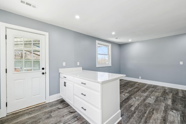 interior space with dark wood finished floors, visible vents, white cabinetry, a peninsula, and baseboards