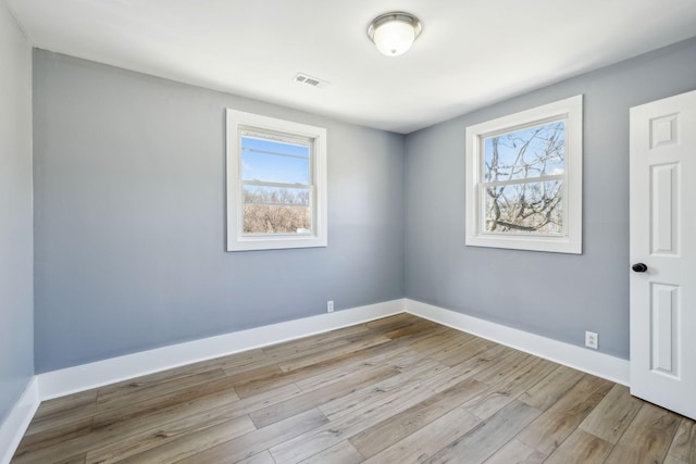 empty room with wood finished floors, visible vents, and baseboards