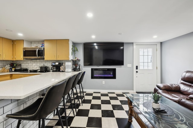 kitchen featuring tile patterned floors, open floor plan, light countertops, decorative backsplash, and stainless steel microwave