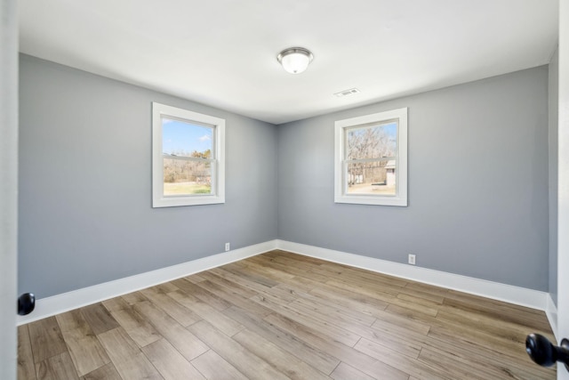 unfurnished room featuring baseboards, visible vents, and wood finished floors