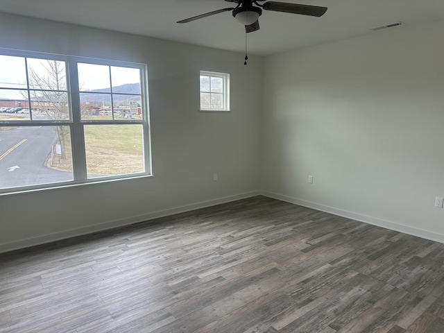 unfurnished room with a ceiling fan, visible vents, baseboards, and wood finished floors