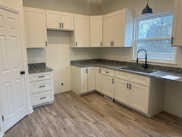 kitchen featuring dark stone counters, white cabinets, decorative light fixtures, light wood-type flooring, and a sink