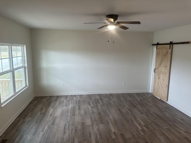 empty room with dark wood-style floors, a barn door, baseboards, and a ceiling fan