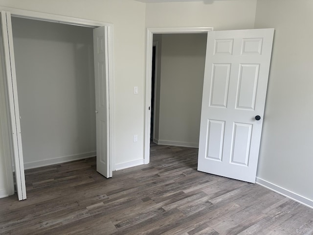 unfurnished bedroom featuring dark wood-style flooring, a closet, and baseboards