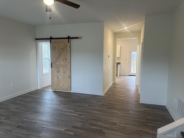 empty room with baseboards, a barn door, a ceiling fan, and dark wood-style flooring