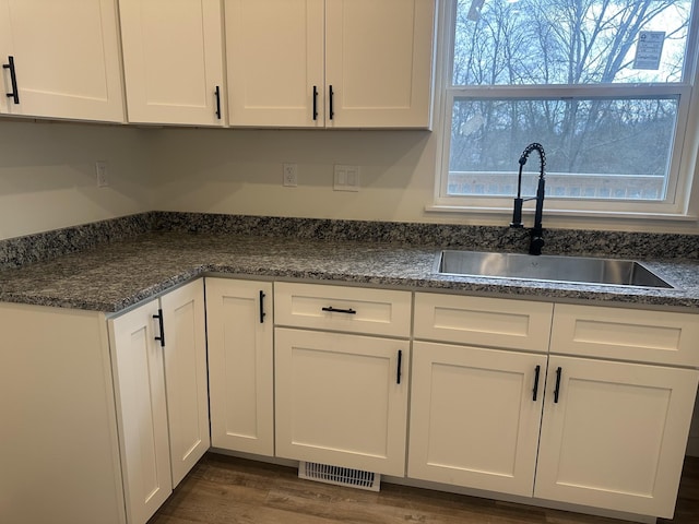 kitchen with dark wood-style flooring, a sink, visible vents, and white cabinets