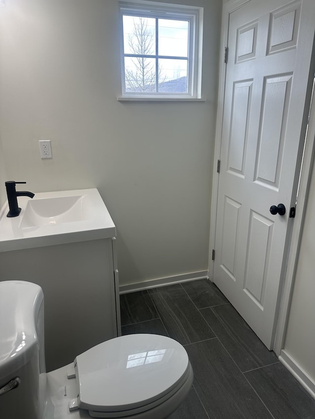 half bathroom featuring toilet, baseboards, and vanity