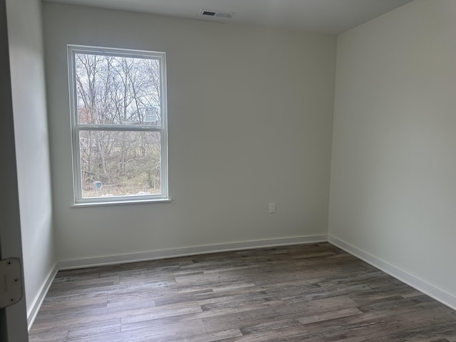 empty room featuring a healthy amount of sunlight, visible vents, baseboards, and wood finished floors