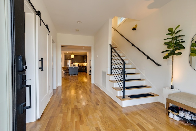 entryway featuring a barn door, stairway, and light wood-type flooring