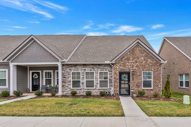 view of front of property with stone siding, a shingled roof, a front yard, and brick siding