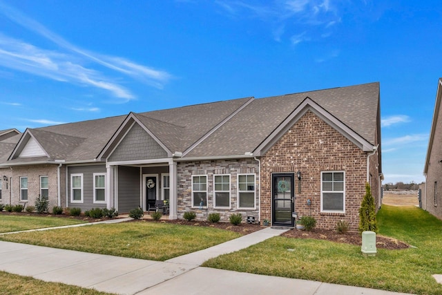 view of front of home featuring stone siding, roof with shingles, a front lawn, and brick siding