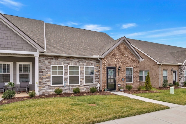 view of front facade with stone siding, a shingled roof, a front lawn, and brick siding