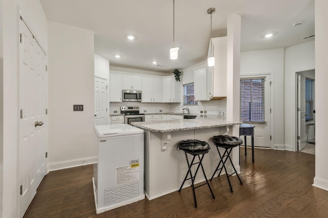 kitchen with appliances with stainless steel finishes, dark wood-type flooring, a peninsula, and decorative backsplash