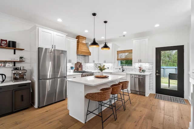 kitchen featuring light wood-type flooring, white cabinetry, premium range hood, and appliances with stainless steel finishes