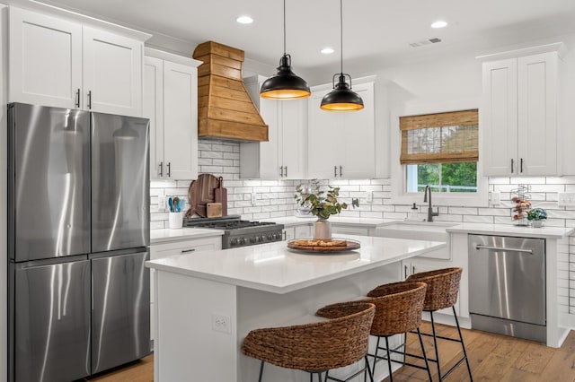 kitchen with stainless steel appliances, white cabinetry, light countertops, a center island, and custom range hood