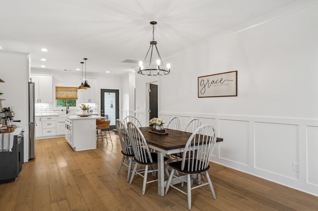 dining room featuring light wood-style floors, a decorative wall, a wainscoted wall, and recessed lighting