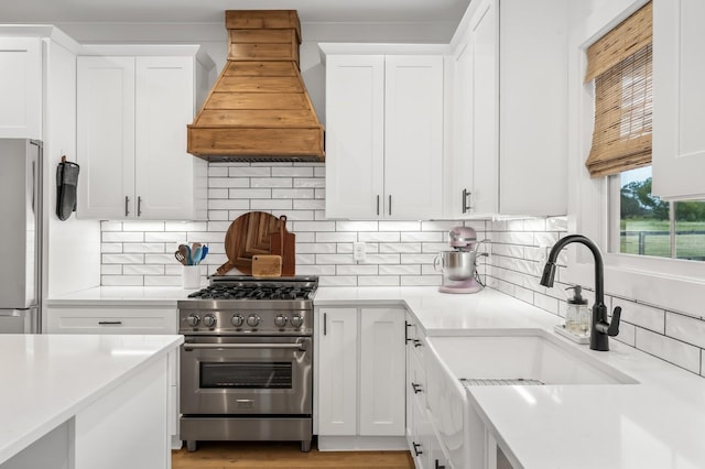 kitchen with appliances with stainless steel finishes, custom range hood, a sink, and white cabinetry