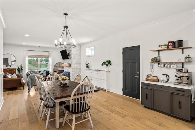 dining space featuring light wood-style floors, a large fireplace, a chandelier, and crown molding