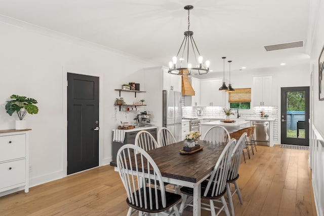 dining space with light wood-type flooring, baseboards, visible vents, and crown molding