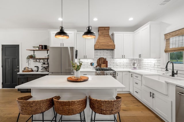 kitchen featuring custom range hood, a kitchen breakfast bar, stainless steel appliances, light wood-style floors, and a sink