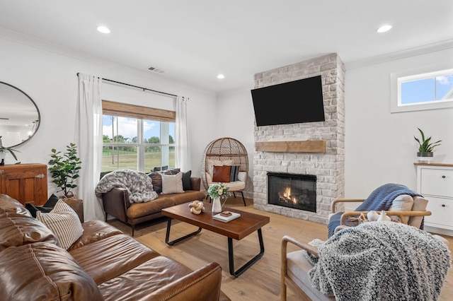 living room with visible vents, ornamental molding, a stone fireplace, light wood-type flooring, and recessed lighting