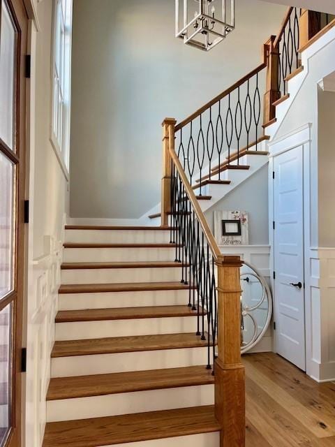 stairs featuring a wainscoted wall, a decorative wall, wood finished floors, and a chandelier