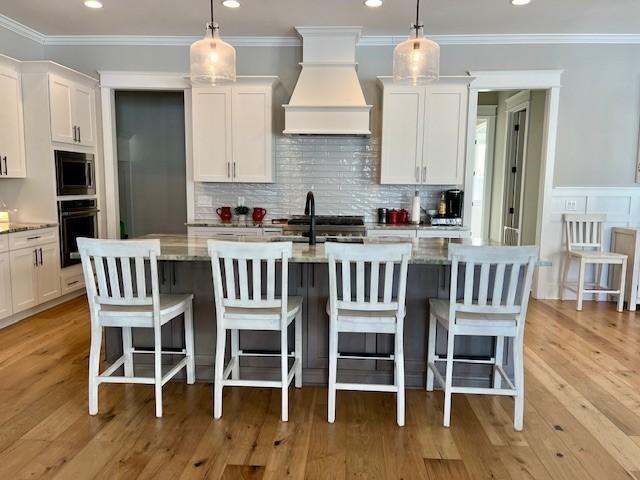 kitchen with custom range hood, stainless steel microwave, light wood-style flooring, white cabinetry, and oven