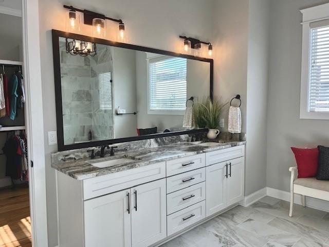 bathroom with a walk in closet, marble finish floor, double vanity, a sink, and a shower stall