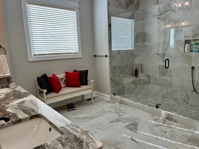 bathroom featuring a stall shower, marble finish floor, baseboards, and double vanity